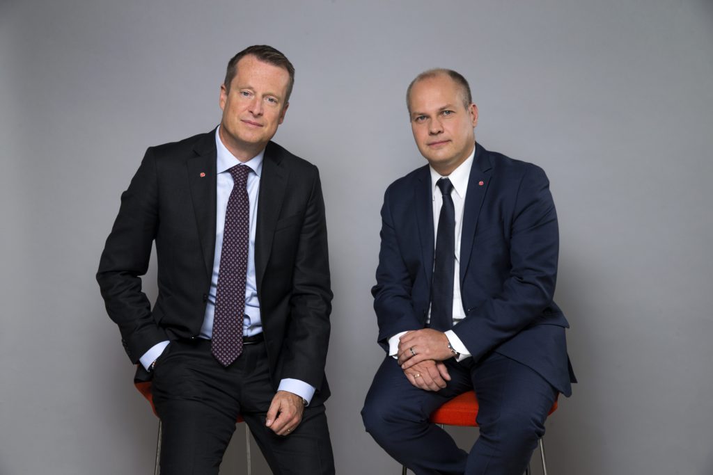 Två män i kostymer och slips som sitter på varsin pall.