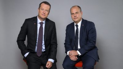 Två män i kostymer och slips som sitter på varsin pall.