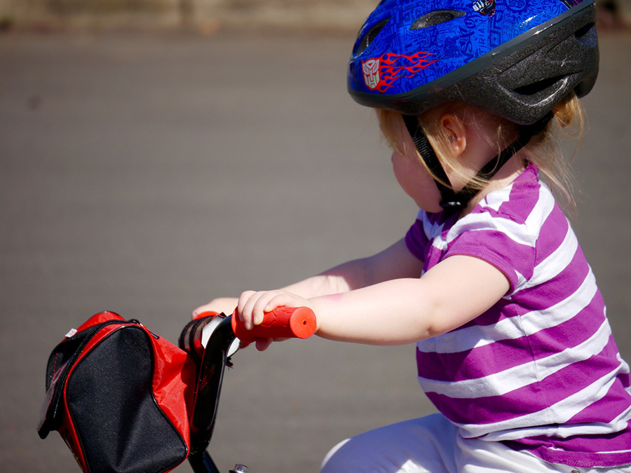Ett litet barn, kanske 3-4 år, som sitter på en liten cykel. Barnet har hjälm och randig tröja.