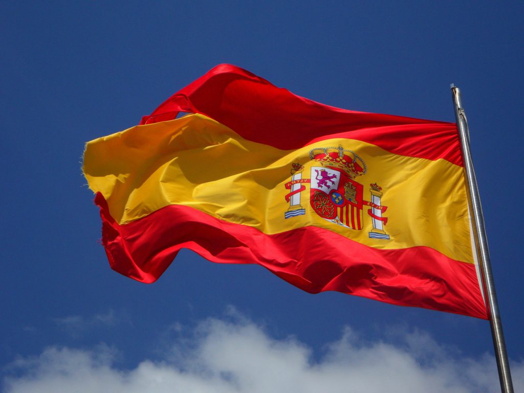 Spaniens flagga som är tre ränder, två röda och en gul i mitten. På den gula randen finns också en bild.
