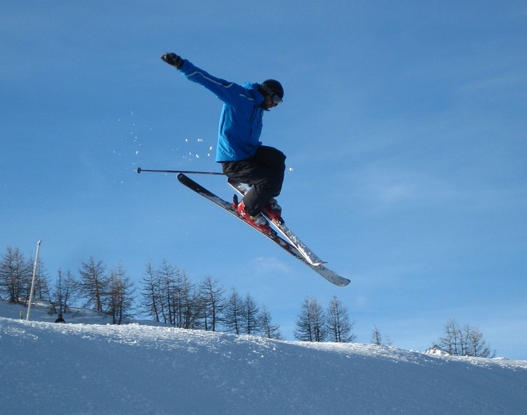 En skidåkare i blå jacka hoppar med sina skidor och armarna utsträckta