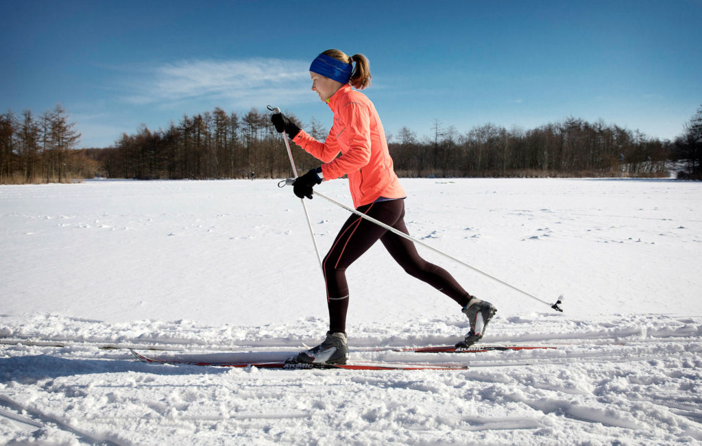 Motionsklädd skidåkare glider fram genom snö under klarblå himmel.