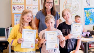 Chefredaktör Marie Hillbom står bakom Astrid, Emelie och Viktor som visar upp sina diplom. De står i ett klassrum.