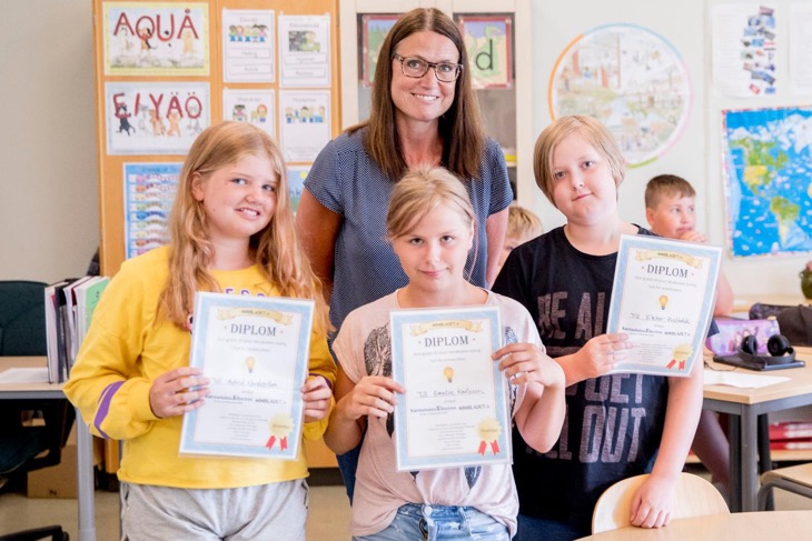 Chefredaktör Marie Hillbom står bakom Astrid, Emelie och Viktor som visar upp sina diplom. De står i ett klassrum.