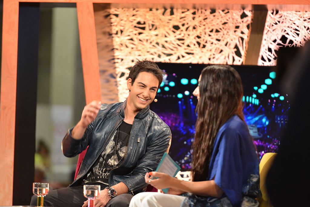 Bild på Darin som sitter i en fåtölj och blir intervjuad. Han skrattar och gör en gest med handen.