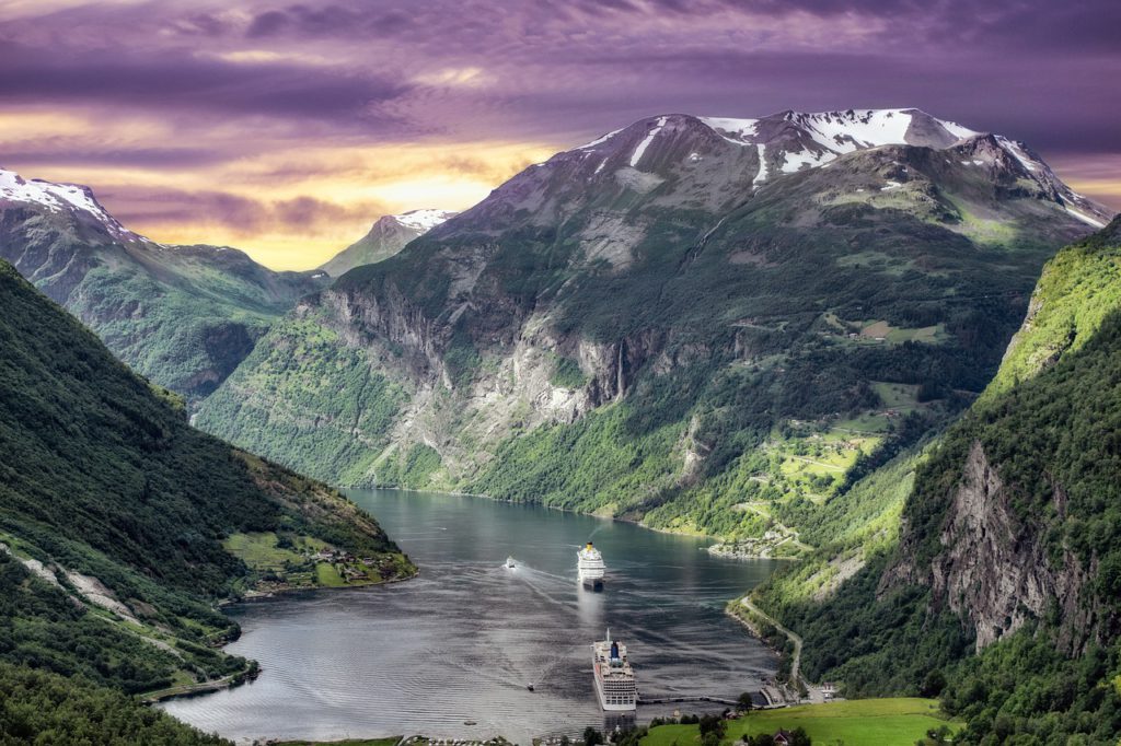 Bild på en fantastik utsikt över en fjord i Norge. Det är solnedgång bakom bergen och i vattnet ligger två stora båtar.