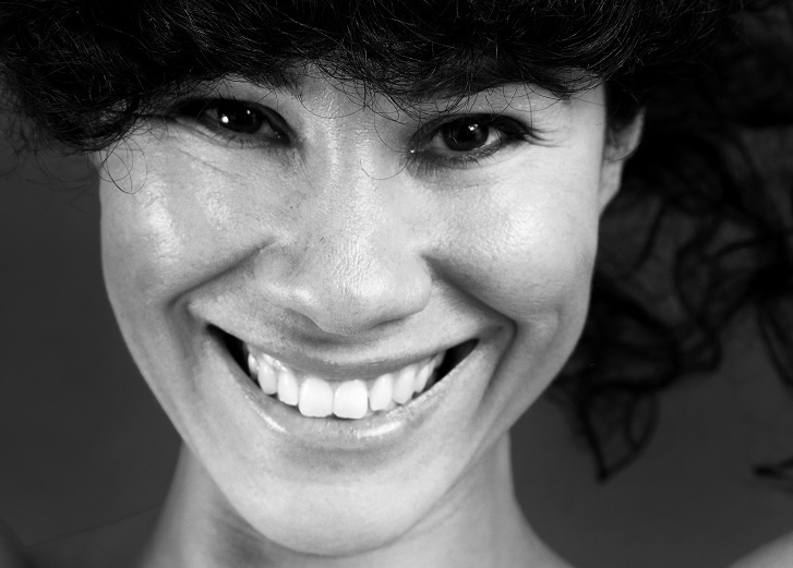 Miriam ler stort mot kameran. Hon har mörk lockigt hår som faller ner i pannan. Ögonen glittrar.