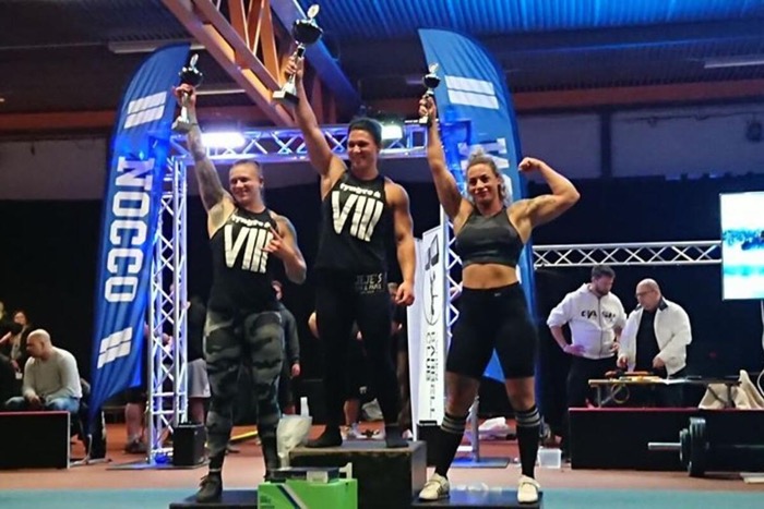 Martina står på medaljpodiet och lyfter upp en pokal i luften.