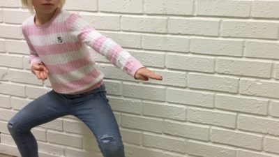 Ung tjej visar ett karateslag framför en vit tegelvägg.