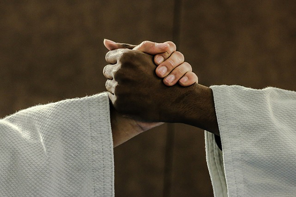 Två personer som har judodräkter på sig och skakar hand. Bara armarna syns.