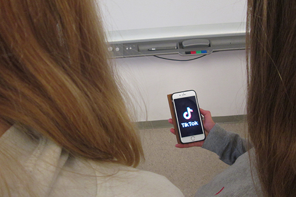 Två elever som tittar på en mobiltelefon som visar appen Tiktok.
