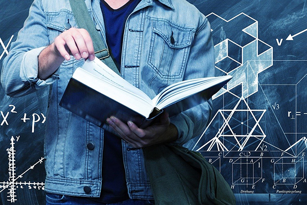 En person som bläddrar i en tjock bok framför en svart tavla med mattetal på.